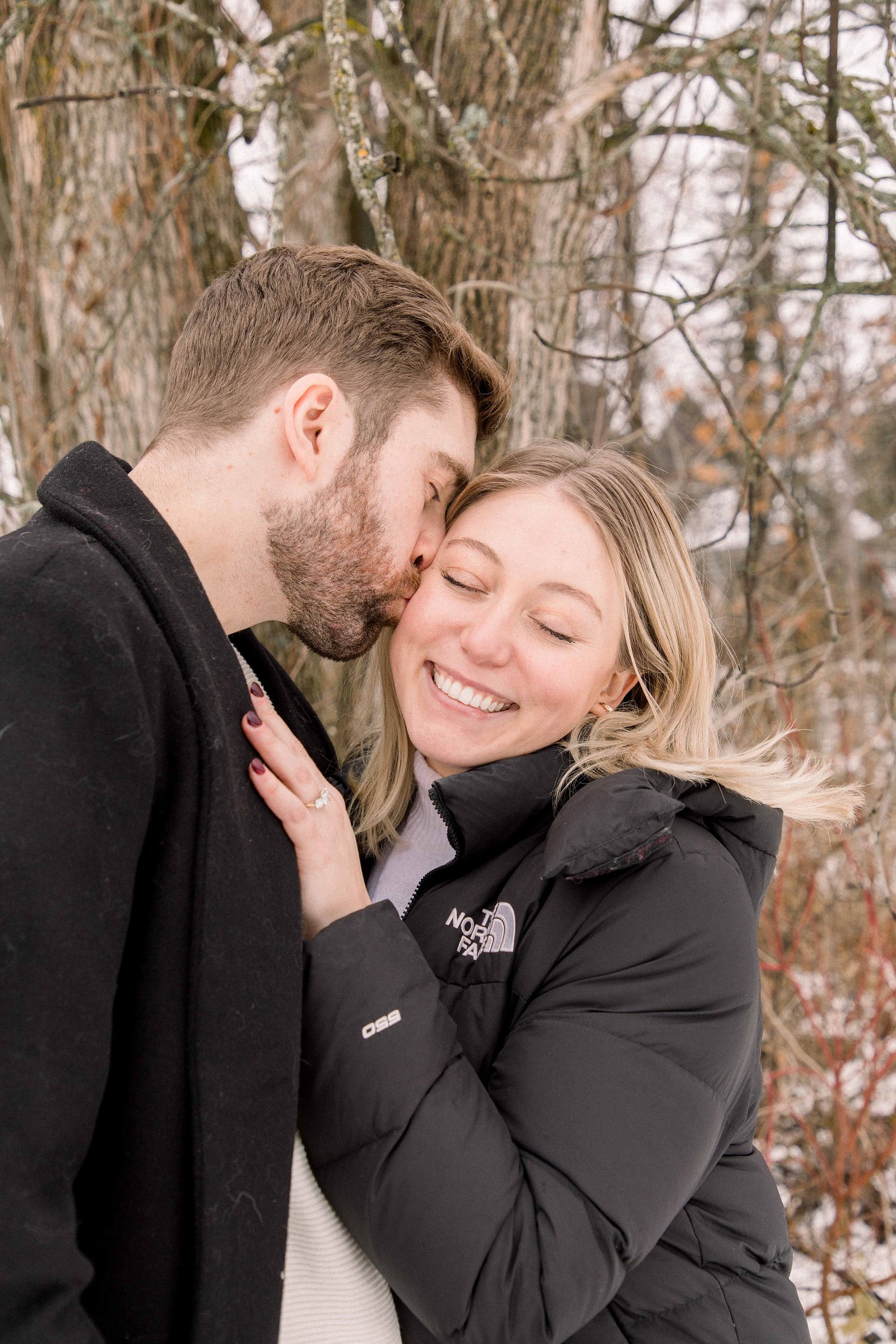 Outdoor Portrait of couple, man giving kiss on woman's cheek. Surprise Proposal. Proposing. Christmas Photos. Ottawa Photographer. Vankleek Hill Photographer. Champlain Photographer. Emily VanderBeek Photography. Candid photography.