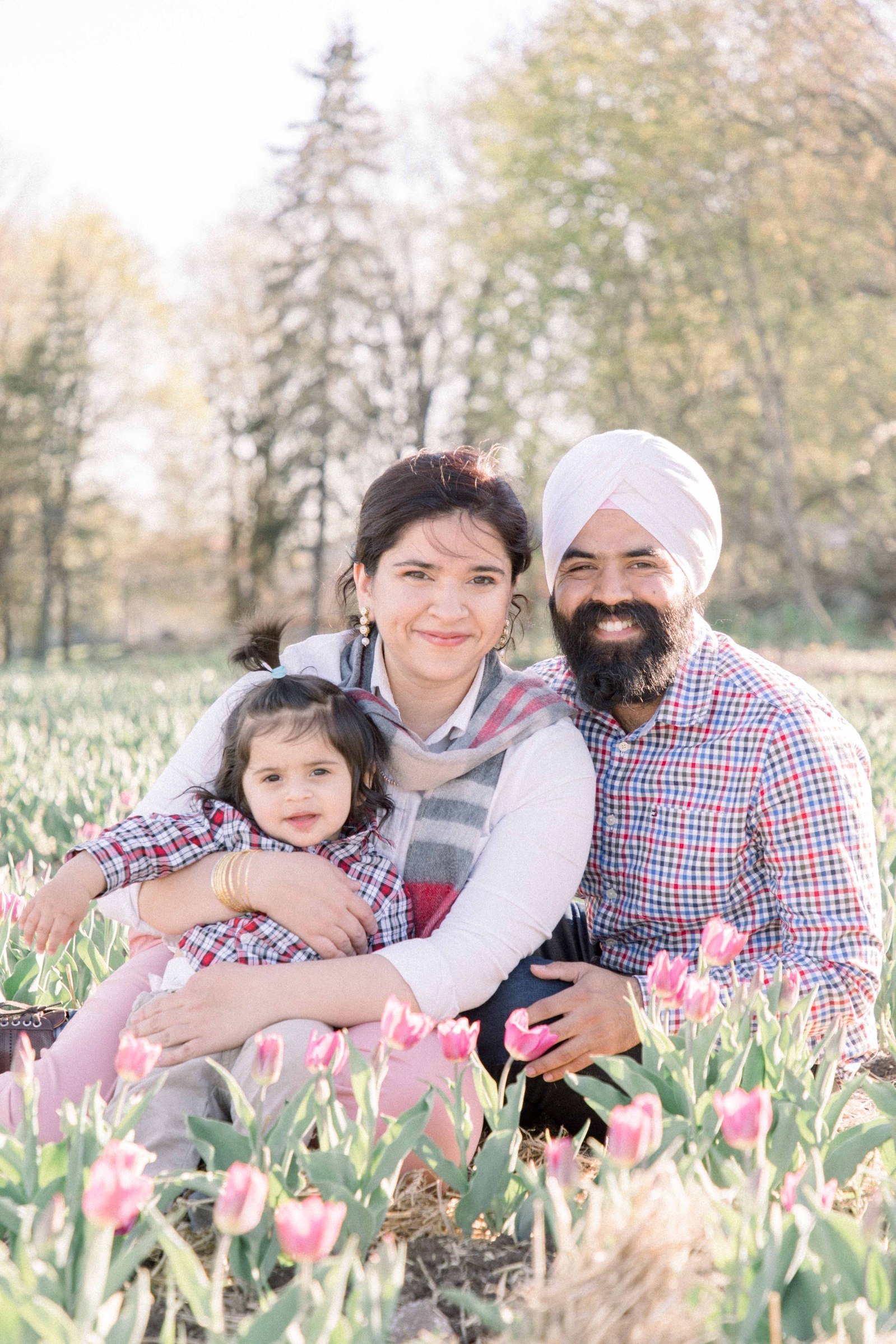Portrait of family of three sitting in a tulip field, looking at the camera and smiling. Vankleek Hill Portrait Photographer, L'Orignal, Champlain, Prescott-Russell, Family Photography, Candid Photography, Emily VanderBeek Photography.