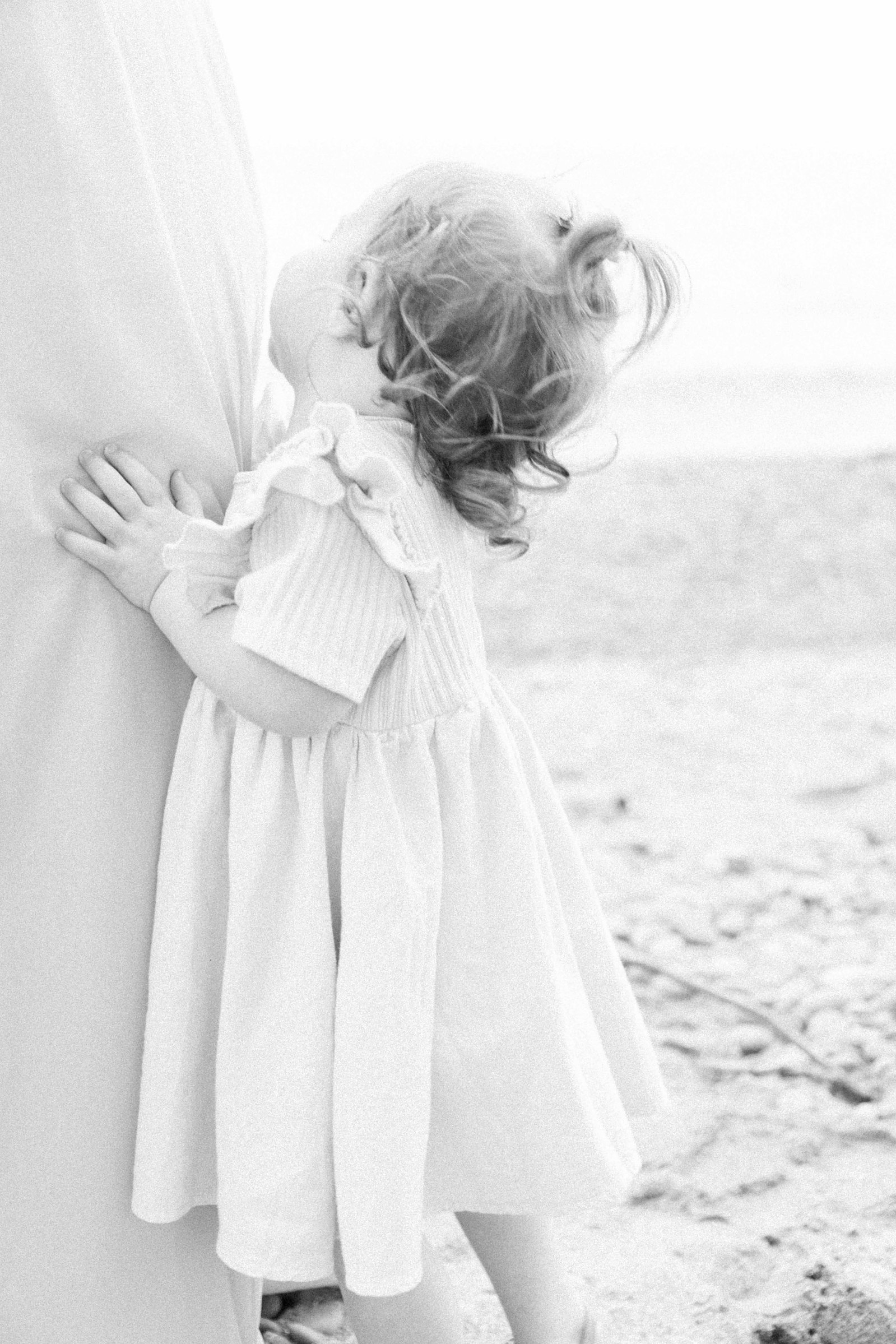 Black and white portrait of a little girl on the beach looking up at her mother, Niagara Portrait Photographer, Niagara Family Photographer, Niagara Motherhood Photography, Beach Portrait Photography, Emily VanderBeek Photography.