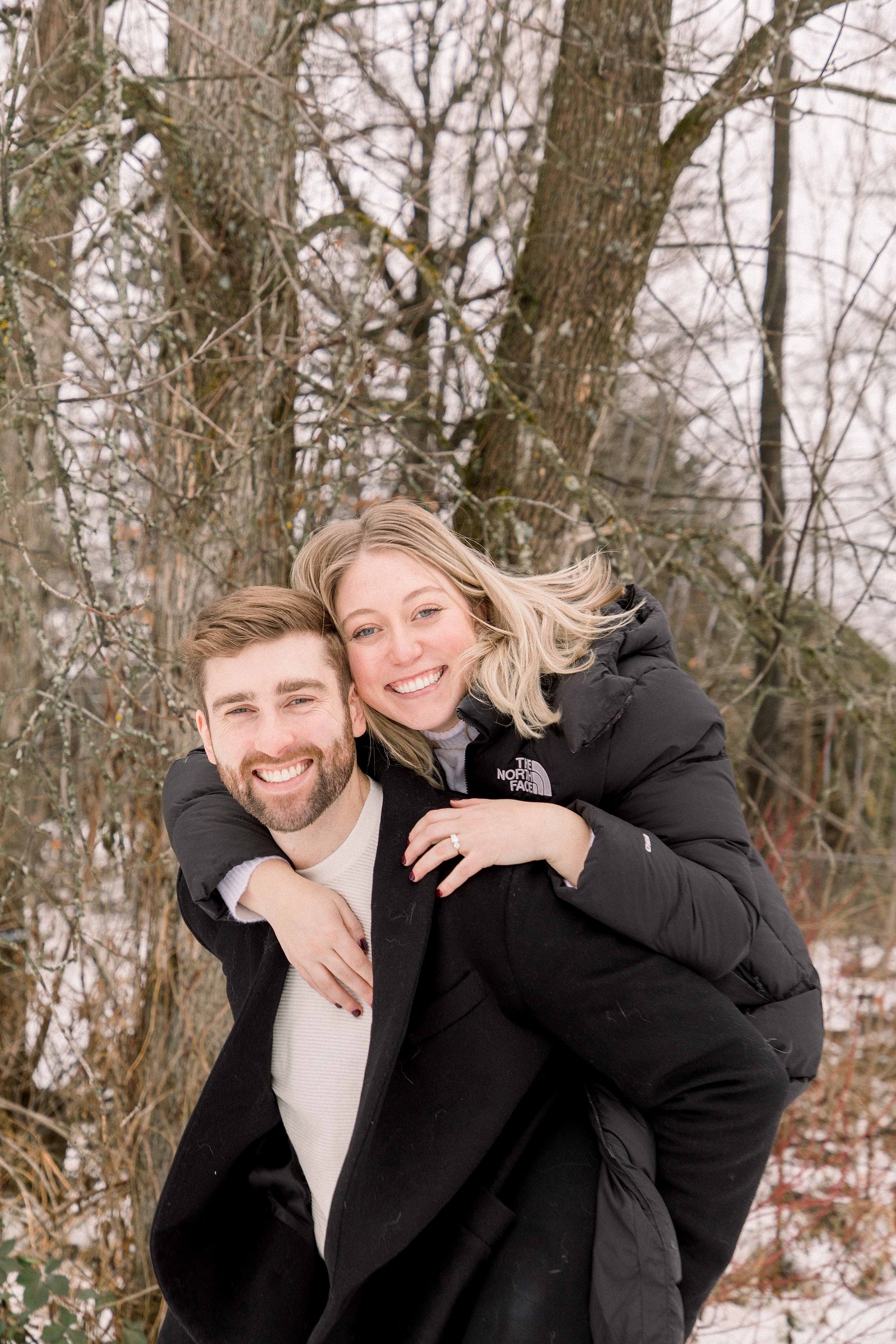 Outdoor Portrait of couple, man giving woman a piggyback. Surprise Proposal. Proposing. Christmas Photos. Ottawa Photographer. Vankleek Hill Photographer. Champlain Photographer. Emily VanderBeek Photography. Candid photography.