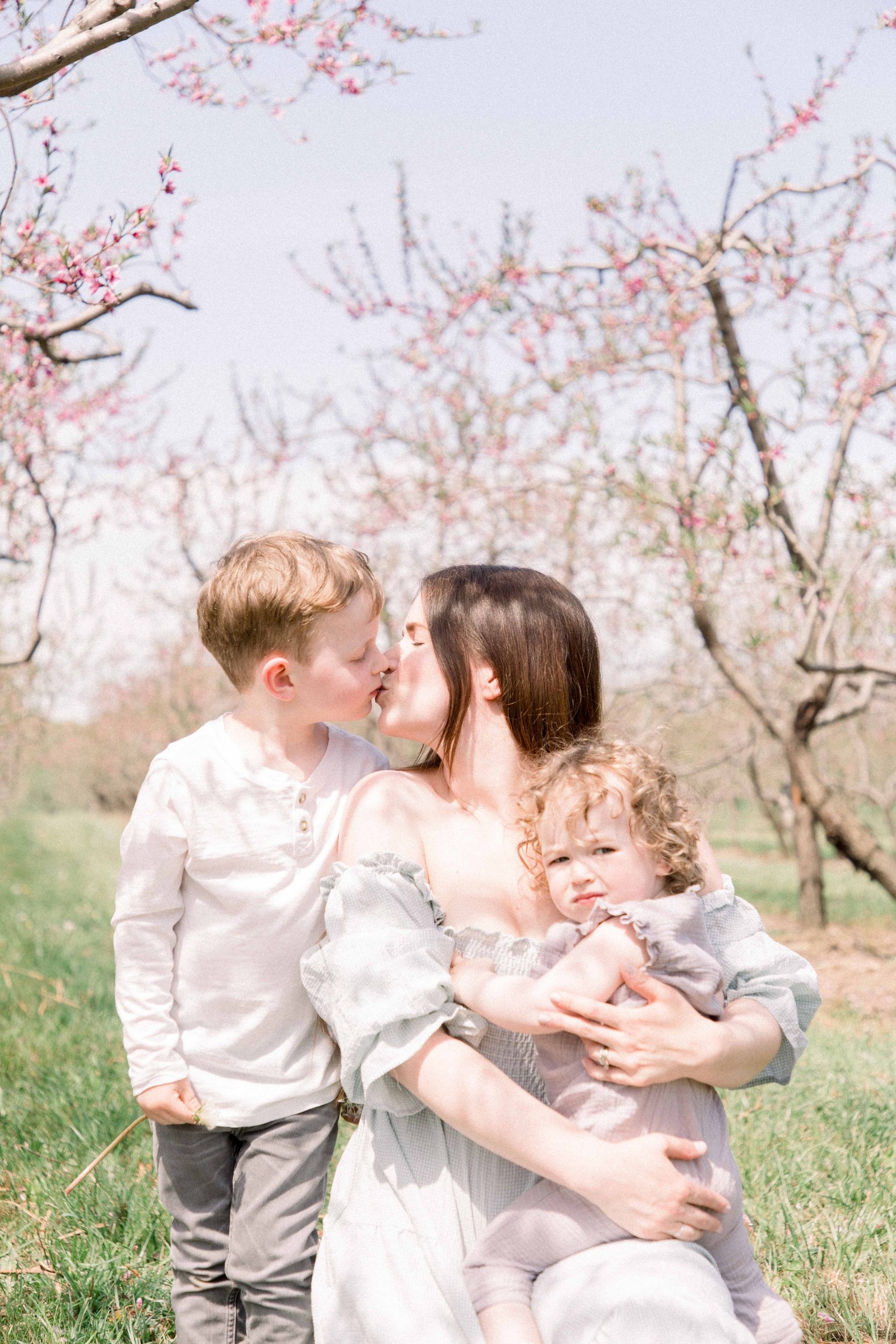 Portrait of mother, baby daughter, and son in an orchard of fruit blossoms. Niagara Family Photographer, Niagara Portrait Photographer, Niagara Motherhood Photographer. Emily VanderBeek Photography, Emily VanderBeek Photo.