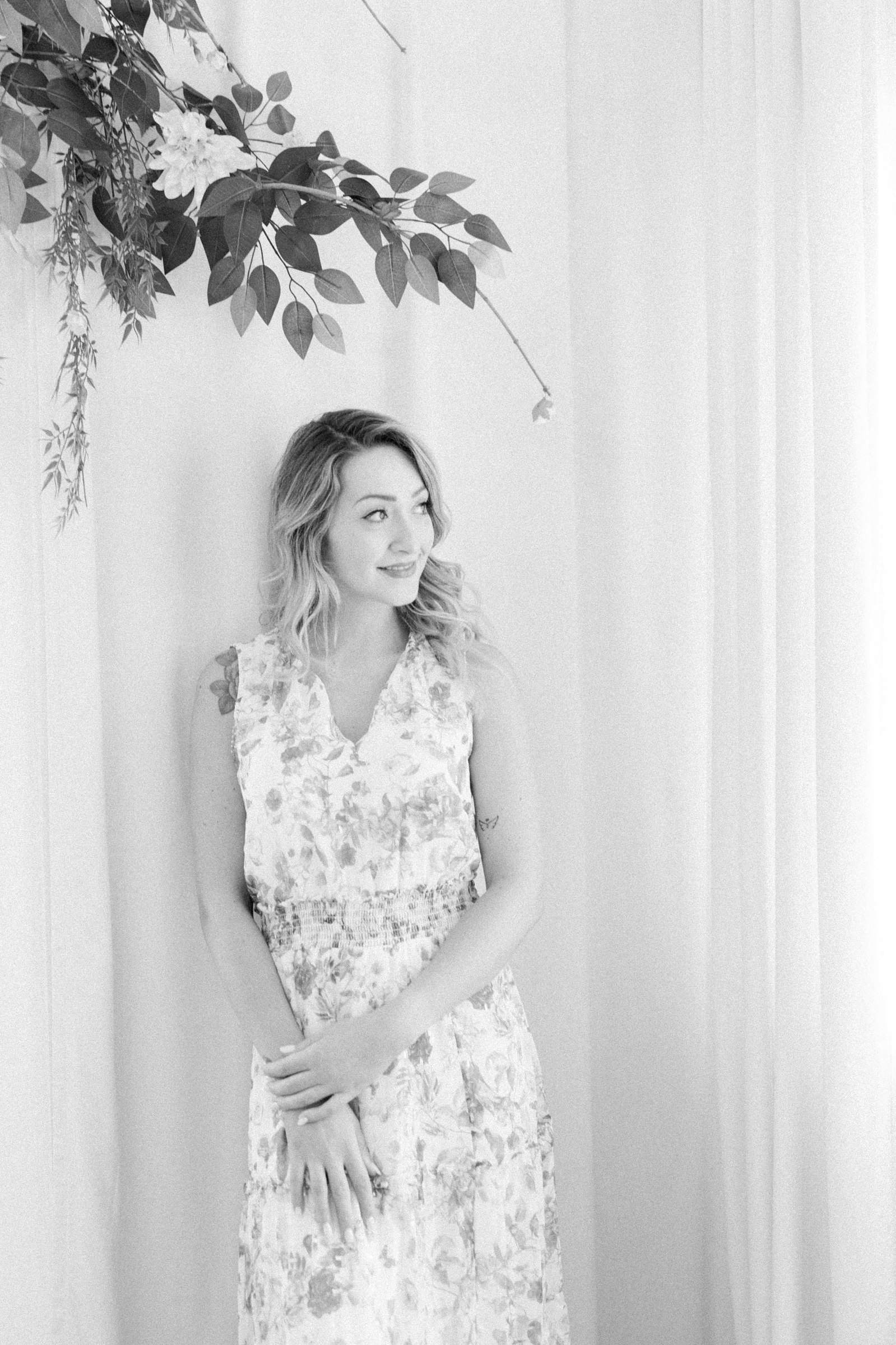 Black and white portrait of a woman standing in front of a studio floral backdrop. Light and airy photography. Emily VanderBeek Photography. Niagara Photographer, Ottawa Photographer, Montreal Photographer.