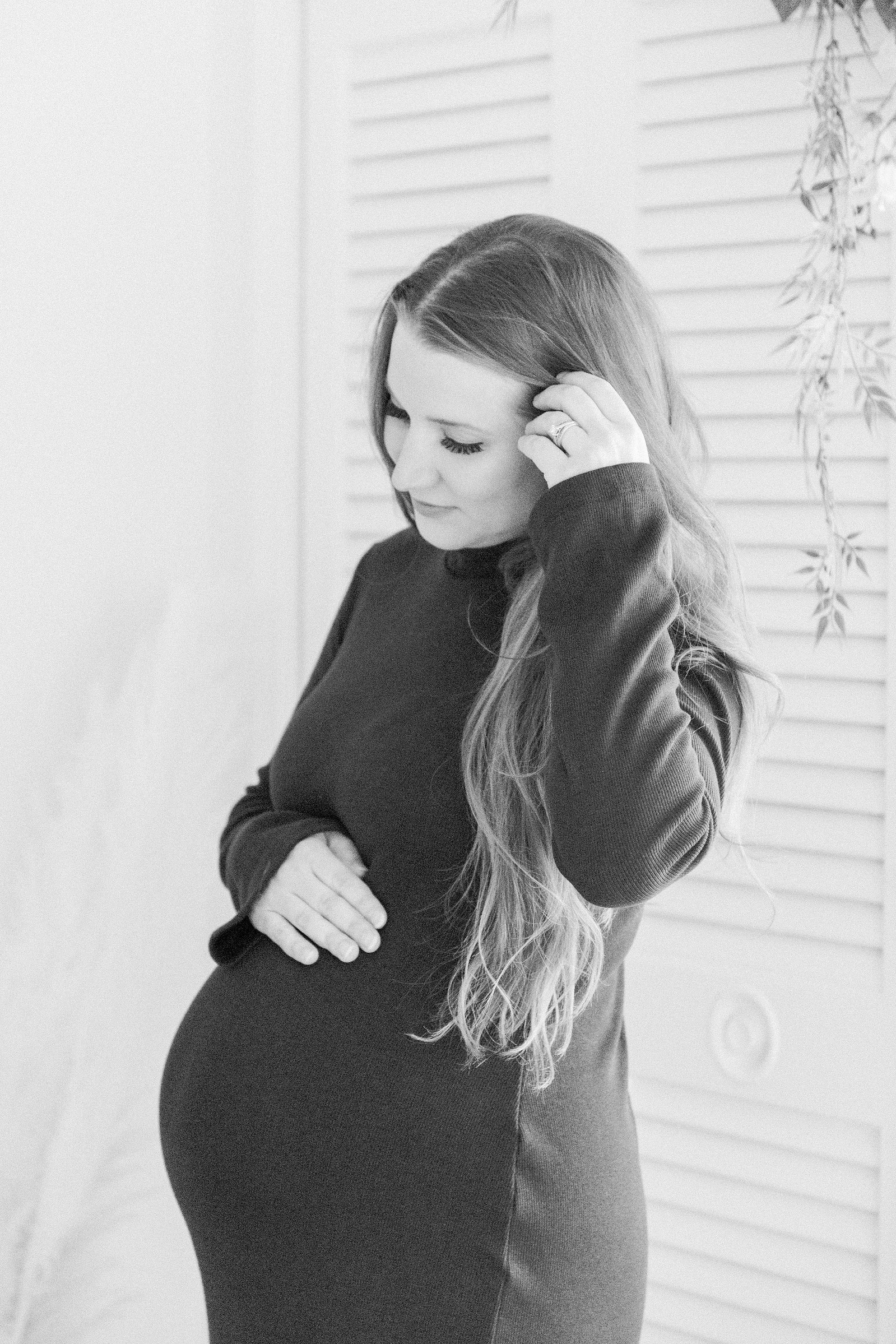 Black & white portrait of a pregnant women holding her belly and looking down at it in a studio. Portrait photography, family photography, motherhood photography, Niagara photographer, Vankleek Hill family photography. Emily VanderBeek Photography.