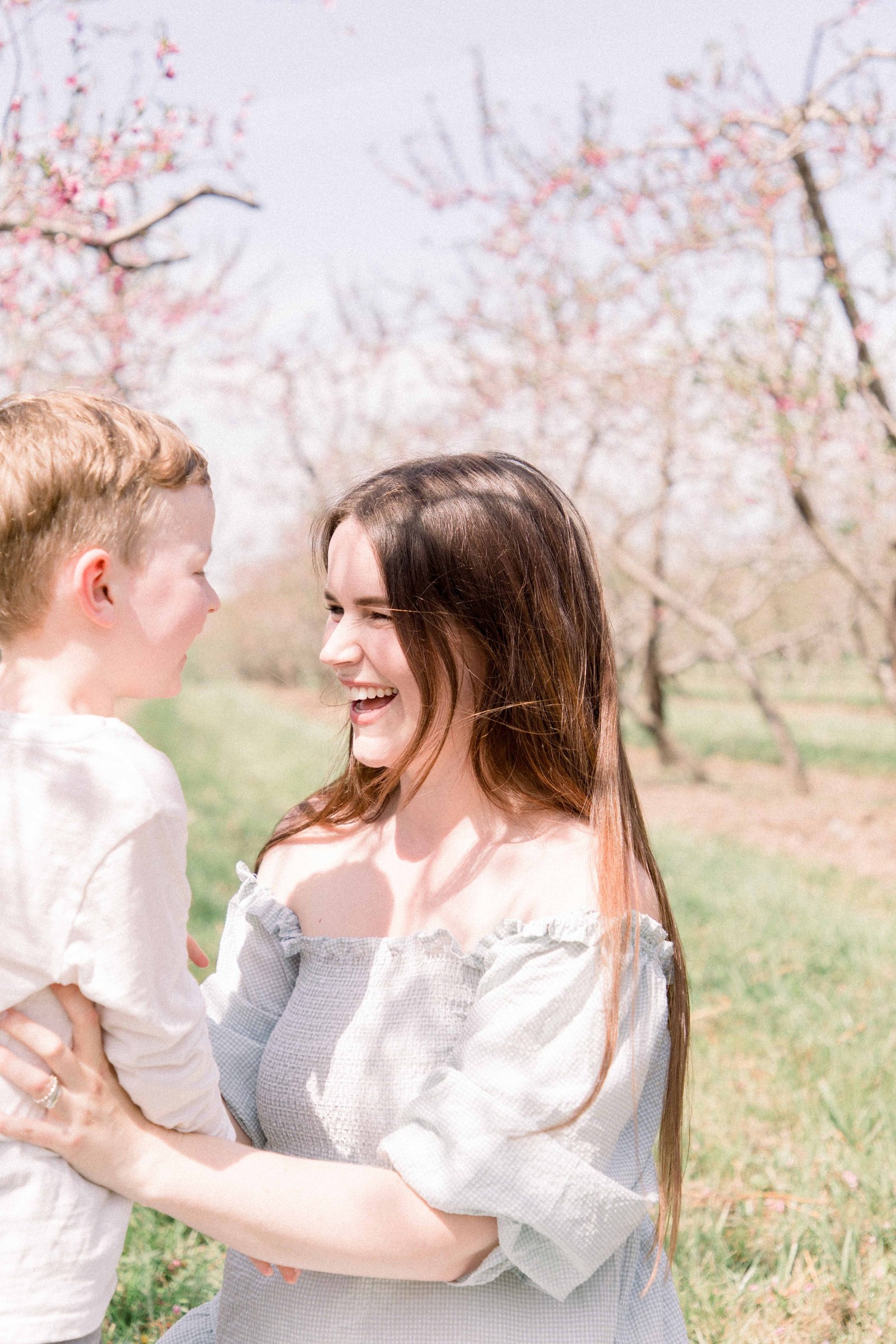 Portrait of mother and son hugging and laughing in an orchard of fruit blossoms. Niagara Family Photographer, Niagara Portrait Photographer, Niagara Motherhood Photographer. Emily VanderBeek Photography, Emily VanderBeek Photo.