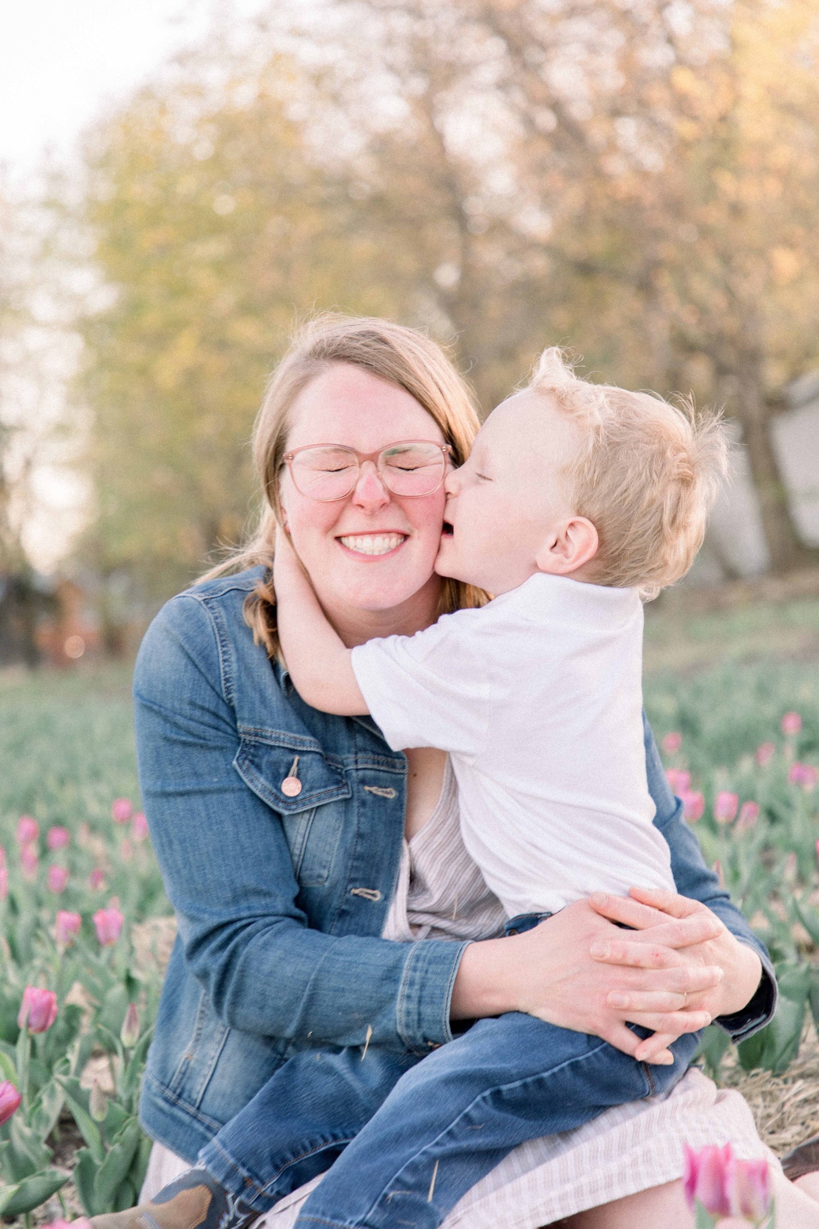 Mother & son sitting in a tulip field. Son gives mom a kiss on the cheek, and mom is smiling. Vankleek Hill Portrait Photographer, L'Orignal, Champlain, Prescott-Russell, Family Photography, Candid Photography, Emily VanderBeek Photography.