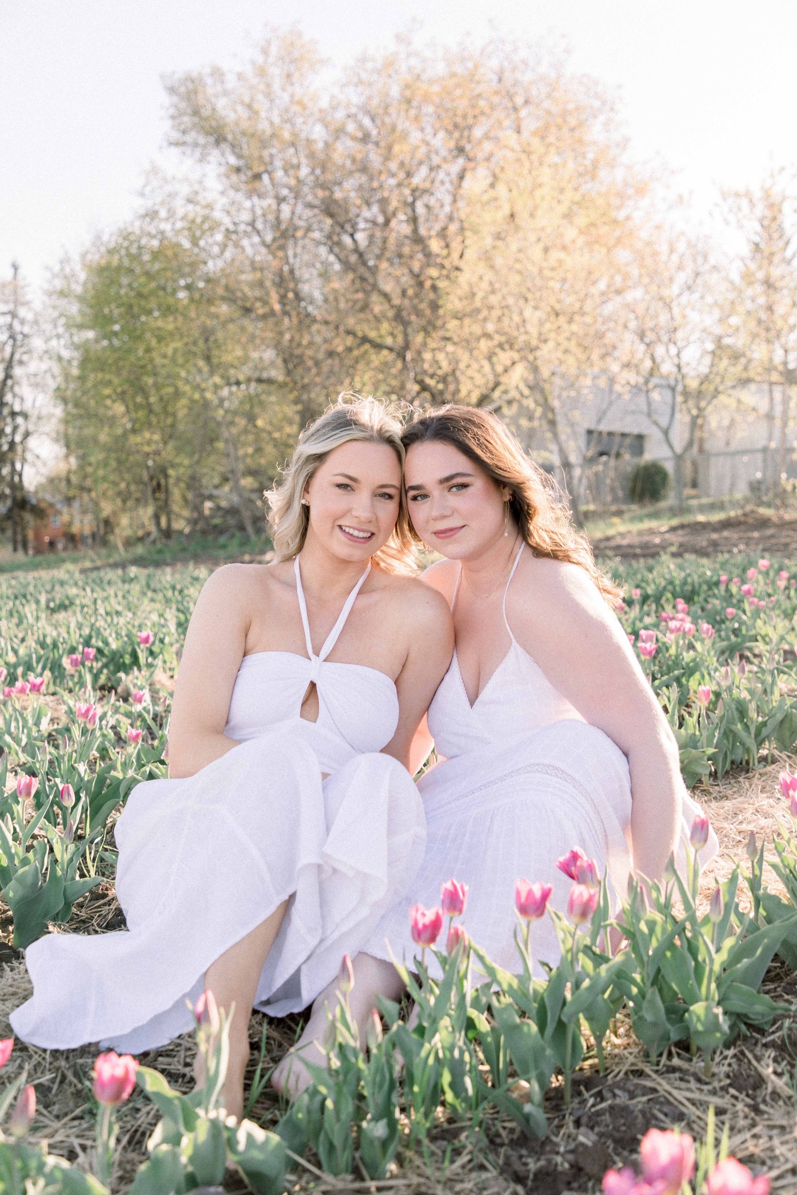 Portrait of two sisters in white dresses with their heads together, looking into the camera. Vankleek Hill Portrait Photographer, L'Orignal, Champlain, Prescott-Russell, Family Photography, Candid Photography, Emily VanderBeek Photography.