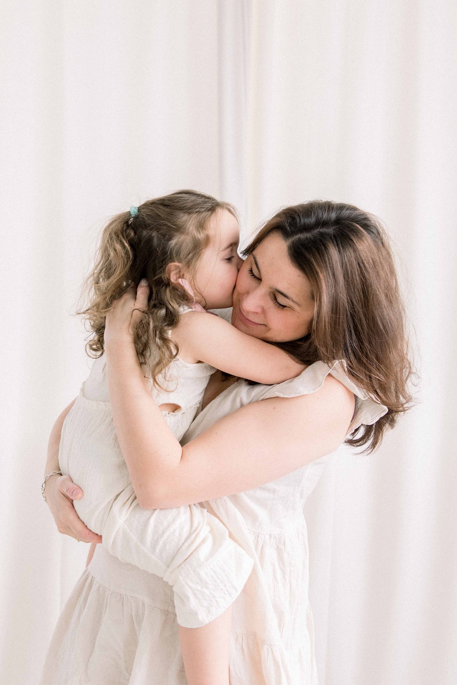 Portrait of a mother and her two babies in a studio. Girl is kissing mom on the cheek. Mom is giving daughter a hug. Emily VanderBeek Photography. Ottawa family photographer. Candid photography.