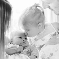 Black and white portrait of a family of four, big sister kissing newborn sister. Emily VanderBeek Photography, Portrait and Family photography, Niagara Photographer, Champlain Photographer, Vaudreuil-Soulanges Photographer, candid photography.