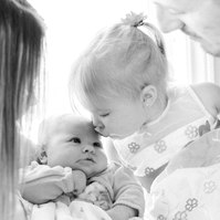 Black and white portrait of a family of four, big sister kissing newborn sister. Emily VanderBeek Photography, Portrait and Family photography, Niagara Photographer, Champlain Photographer, Vaudreuil-Soulanges Photographer, candid photography.