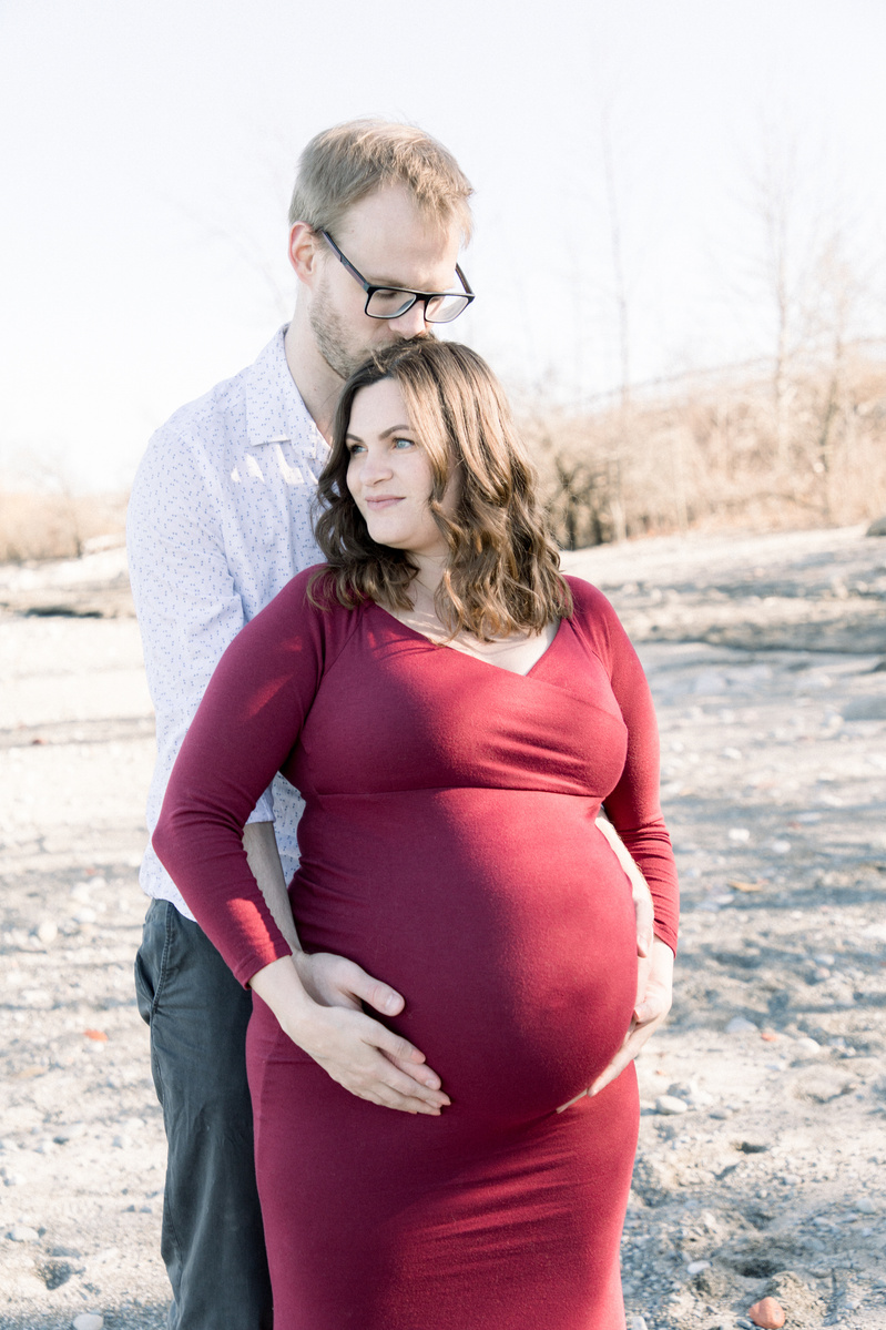 Maternity photo pf man hugging woman from behind on beach, Emily VanderBeek Photography, Portrait and Family photography, Niagara Photographer, Champlain Photographer, Vaudreuil-Soulanges Photographer, candid photography, authentic photography.