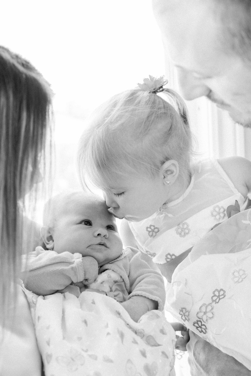 Black and white portrait of a family of four, big sister kissing newborn sister. Emily VanderBeek Photography, Portrait and Family photography, Niagara Photographer, Champlain Photographer, Vaudreuil-Soulanges Photographer, candid photography.