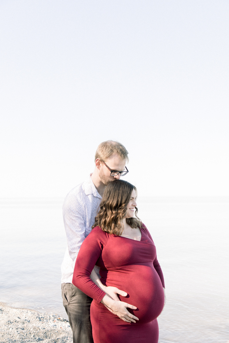 Maternity photo of man hugging woman from behind on beach, Emily VanderBeek Photography, Portrait and Family photography, Niagara Photographer, Champlain Photographer, Vaudreuil-Soulanges Photographer, candid photography, authentic photography.