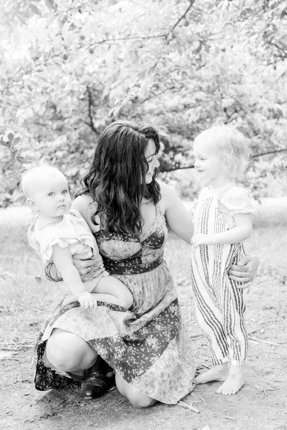 Black and white portrait of mother holding two daughters smiling in orchard, Niagara family photographer, Niagara portrait photographer, family photography, portrait photography, candid photography, authentic photography, Emily VanderBeek Photography.