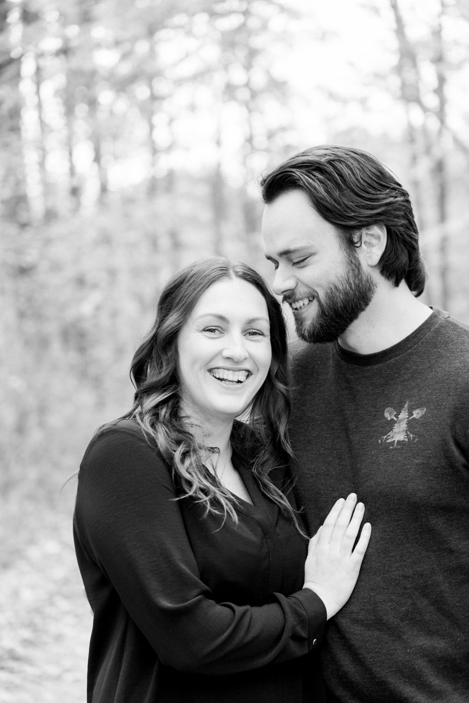 Black and white portrait of couple, man whispering secret to woman, woman looking into the camera, smiling. Niagara portrait photography, Niagara portrait photographer, Niagara family photography, Niagara family photographer.