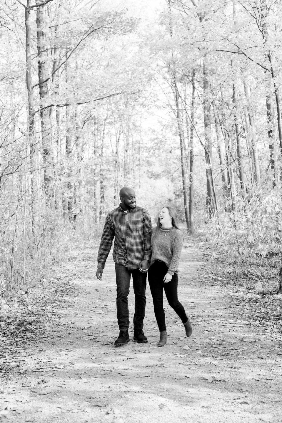 Black and white portrait of couple walking down path, bumping hips and laughing. Niagara portrait photography, Niagara portrait photographer, Niagara family photography, Niagara family photographer.