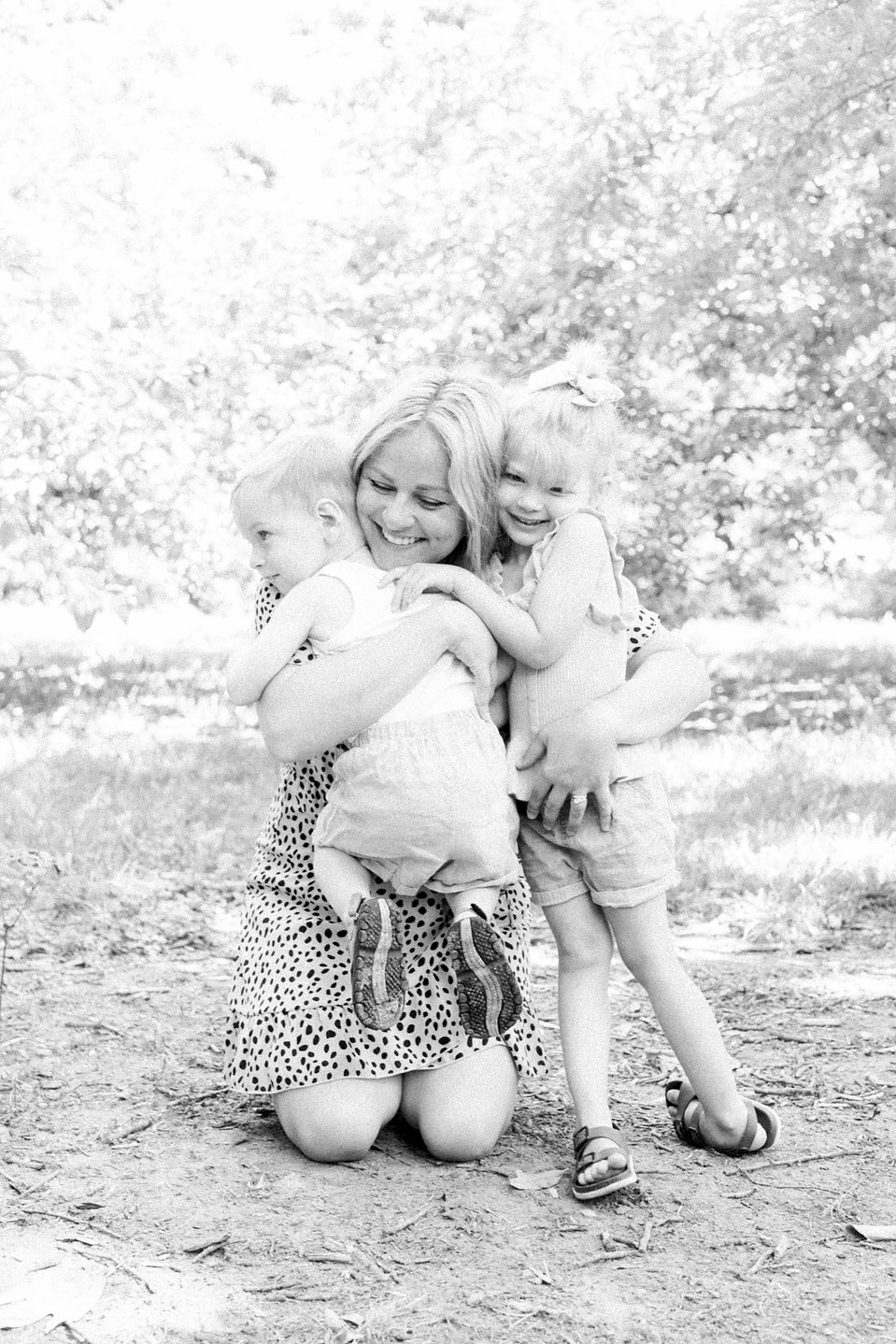 Black and white photo of mother hugging her son and daughter in a fruit orchard, Niagara family photographer, Niagara portrait photographer, family photography, portrait photography, candid photography, authentic photography, Emily VanderBeek Photography.