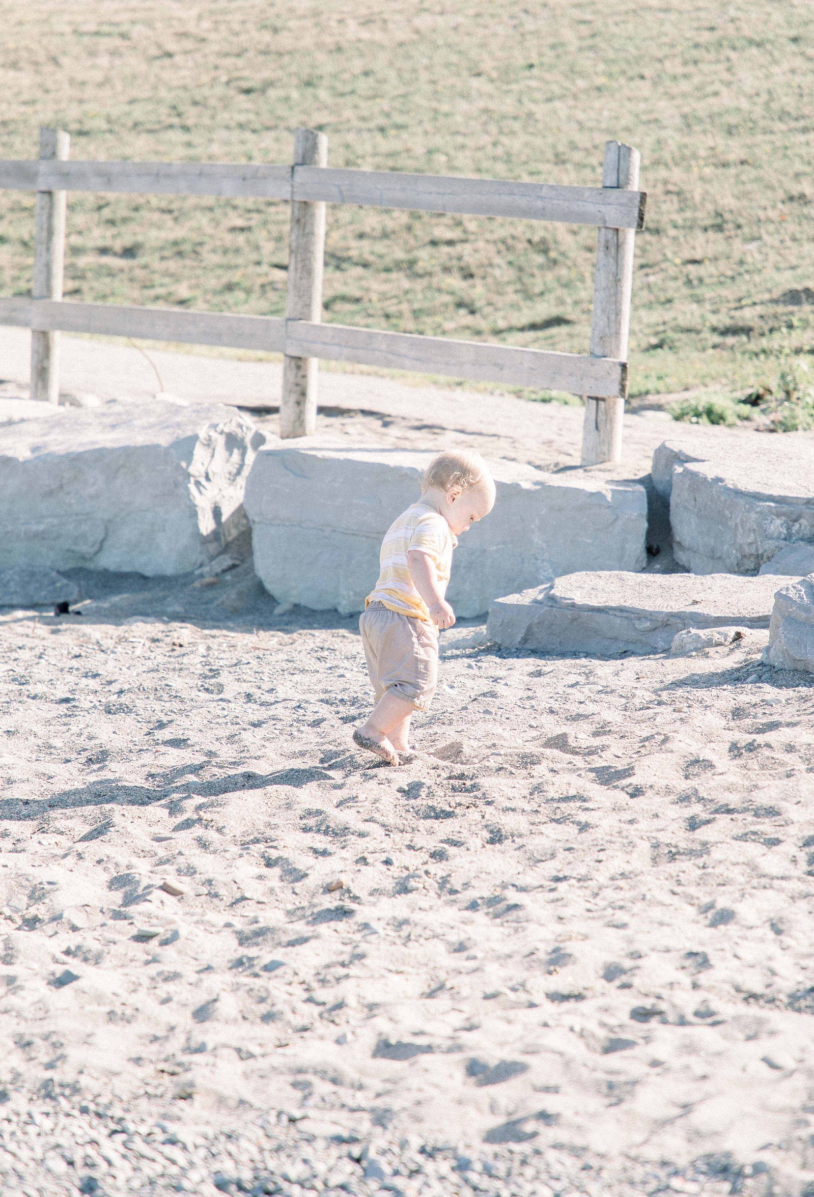 Portrait of toddler boy walking on the beach. Niagara family photographer, Niagara family photography, Niagara portrait photographer, Niagara portrait photography.