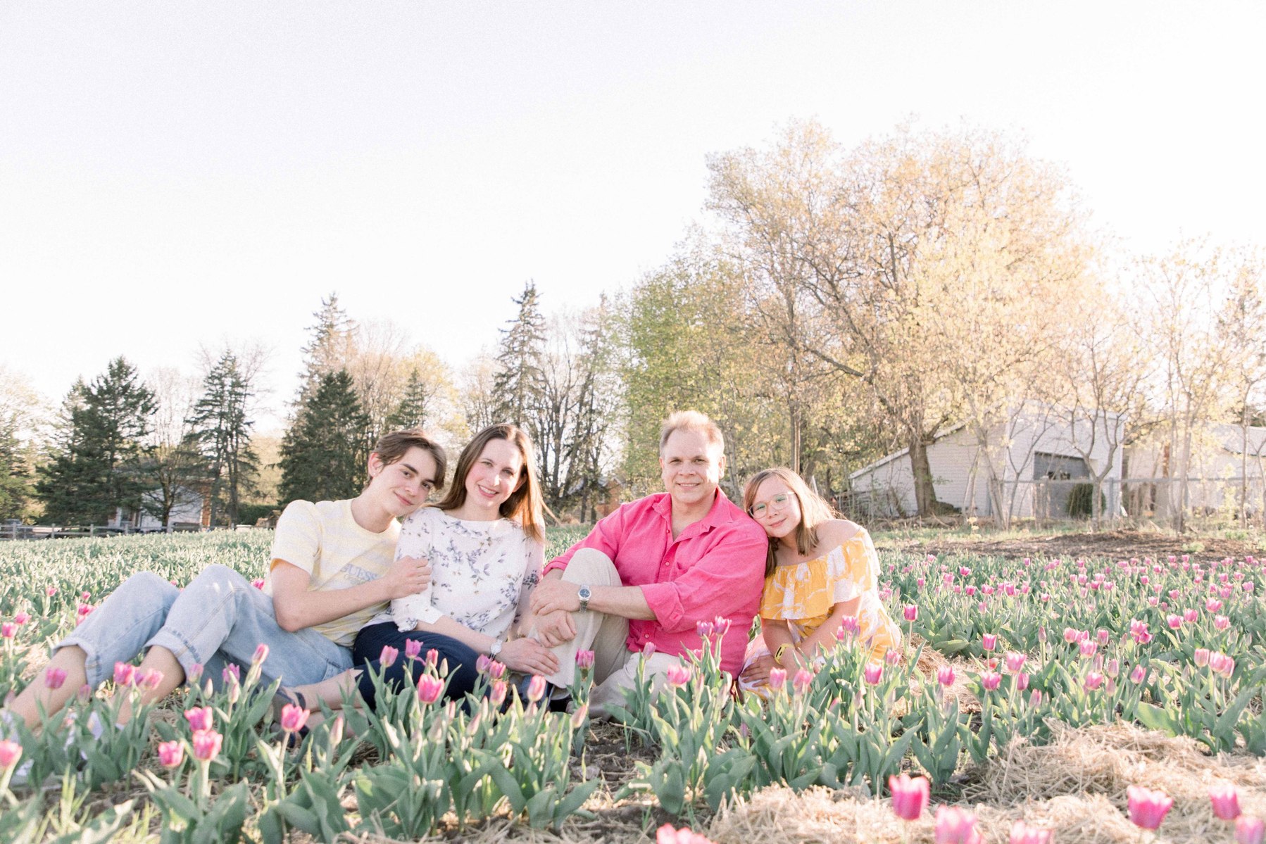 Portrait of a family of four sitting down in a tulip field looking at the camera and smiling. Vankleek Hill Portrait Photographer, L'Orignal, Champlain, Prescott-Russell, Family Photography, Candid Photography, Emily VanderBeek Photography.