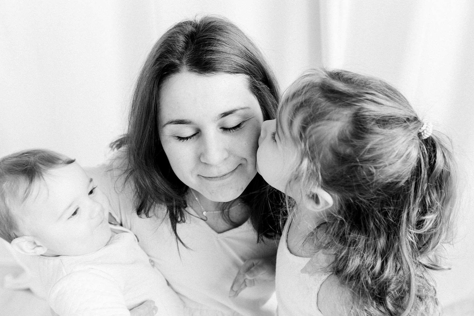 Black & white portrait of a mother and her two babies in a studio. Girl is kissing mom on the cheek. Emily VanderBeek Photography. Ottawa family photographer. Candid photography.
