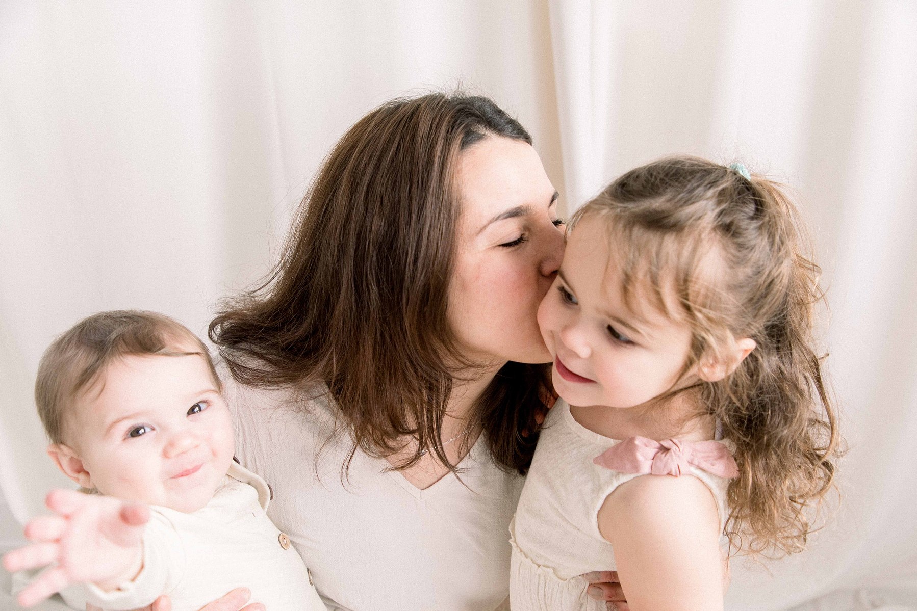 Portrait of a mother and her two babies in a studio. Girl is kissing mom on the cheek. Emily VanderBeek Photography. Ottawa family photographer. Candid photography.