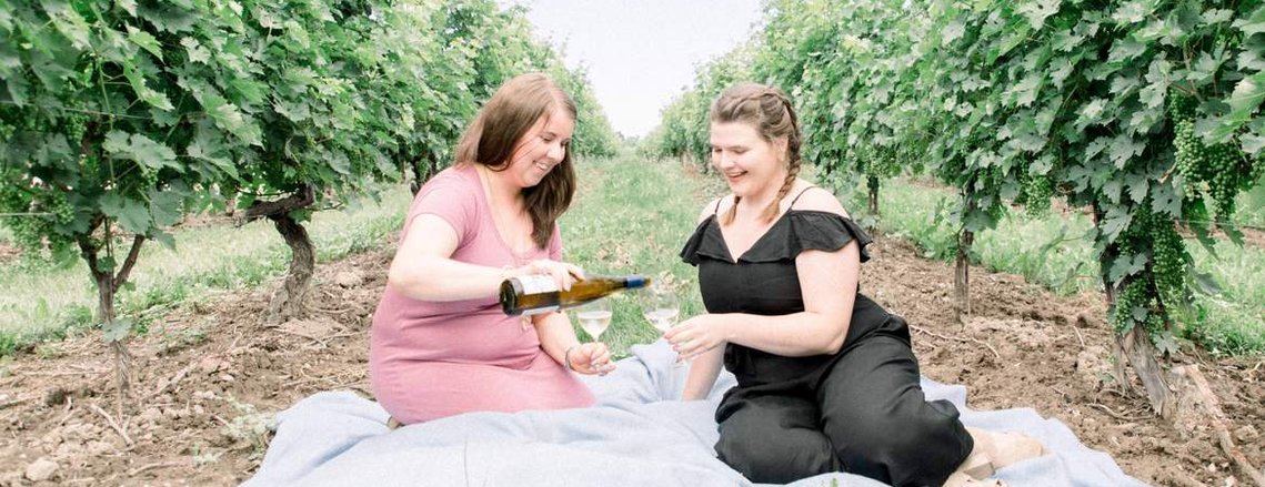 Portrait of two women sitting in vineyard pouring a glass of wine, Emily VanderBeek Photography, Portrait and Family photography, Niagara Photographer, Champlain Photographer, Vaudreuil-Soulanges Photographer, candid photography, authentic photography.