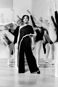 Black and white environmental portrait of a female ballet dance director surrounded by ballet dancers, blurred with slow shutter speed. Photographed in Chicago for Chicago Magazine