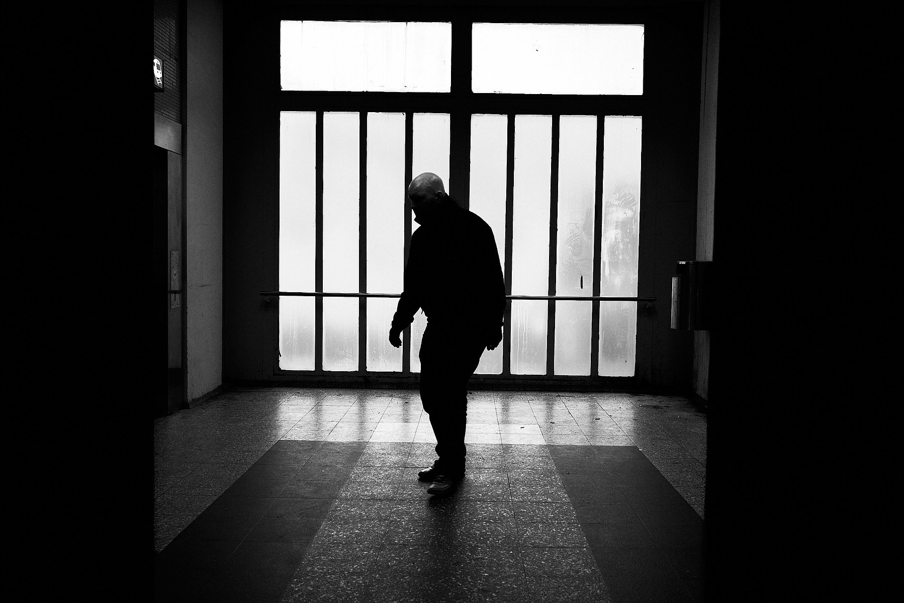 A figure of a bald man wearing pilot jacket walks past a window wall
