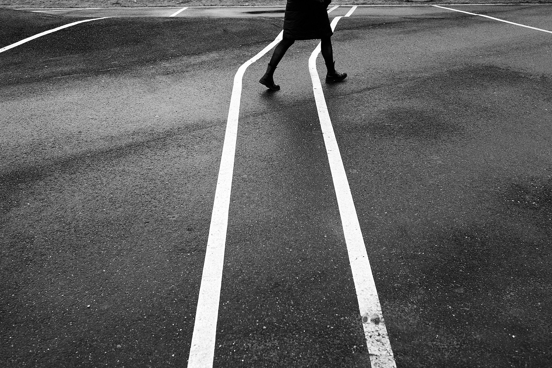 A pedestrian crosses diagonally two white lines painted on street