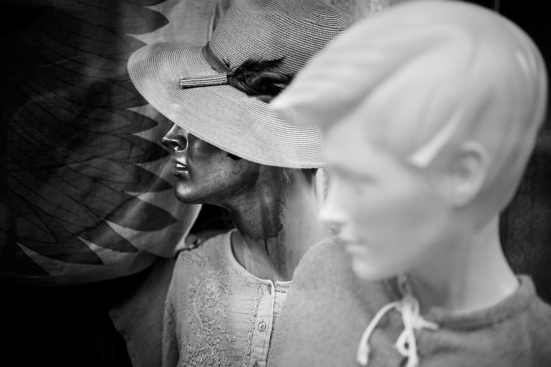 Two mannequin dolls seen though a shop window, the doll in the foreground is painted white, while the face of the doll in the background is painted with gold paint