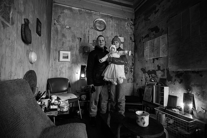 A portrait of a man and woman. They are homeless and take shelter in an abandoned building in Moscow. The woman holds a baby, it is not a real baby it is a toy doll.