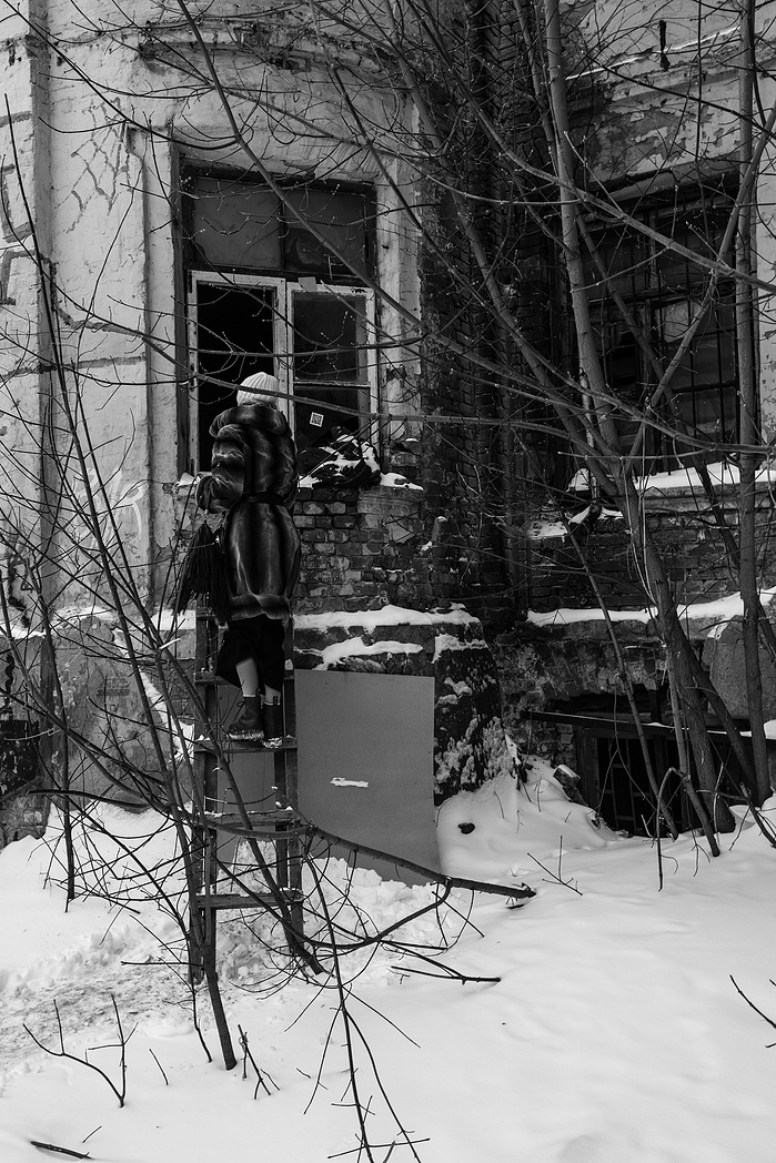 A women climbs a wooden ladder to enter an abandoned building.