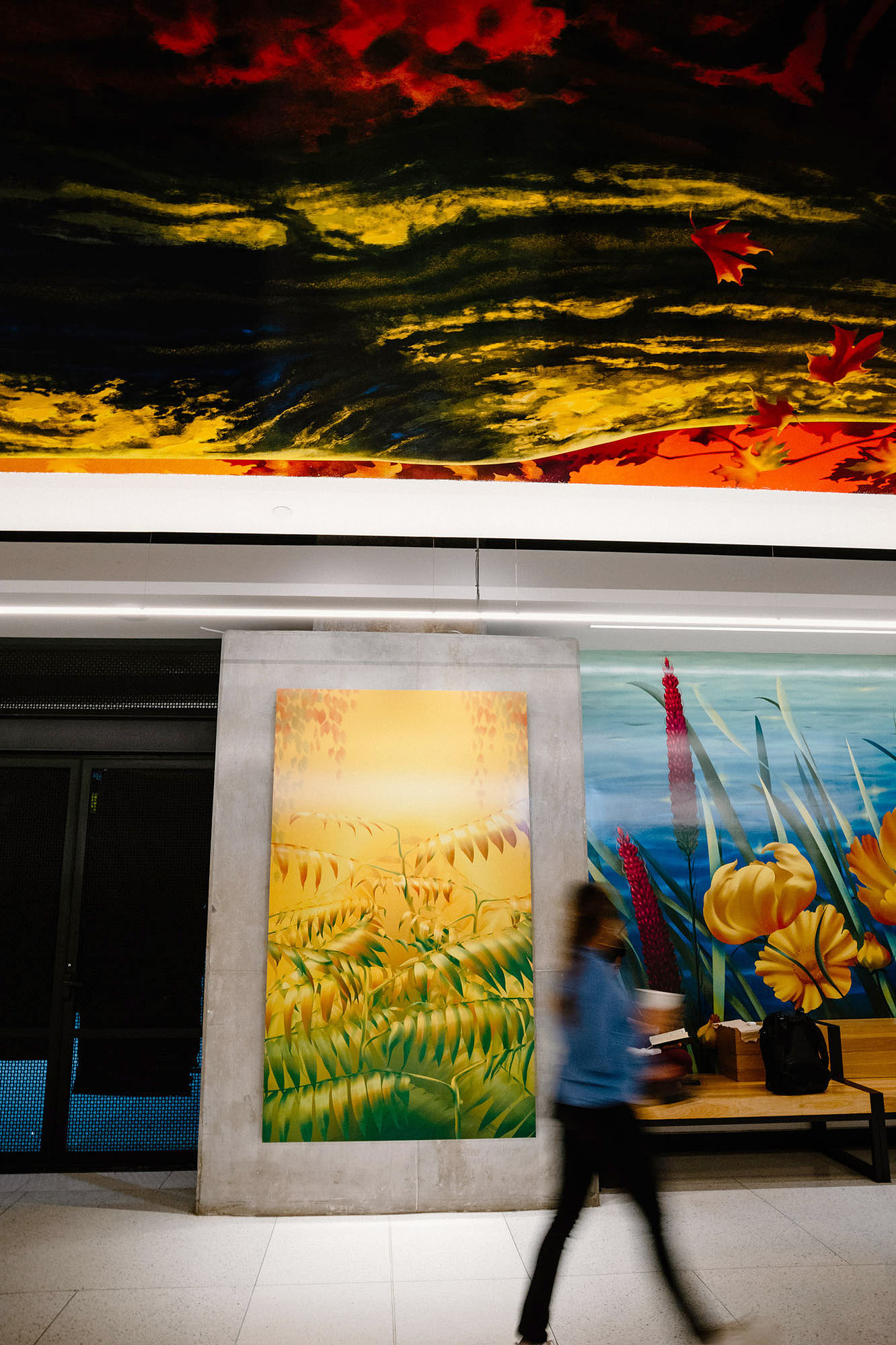 A woman walks across colourful murals and artworks depicting nature and plants in a public setting.