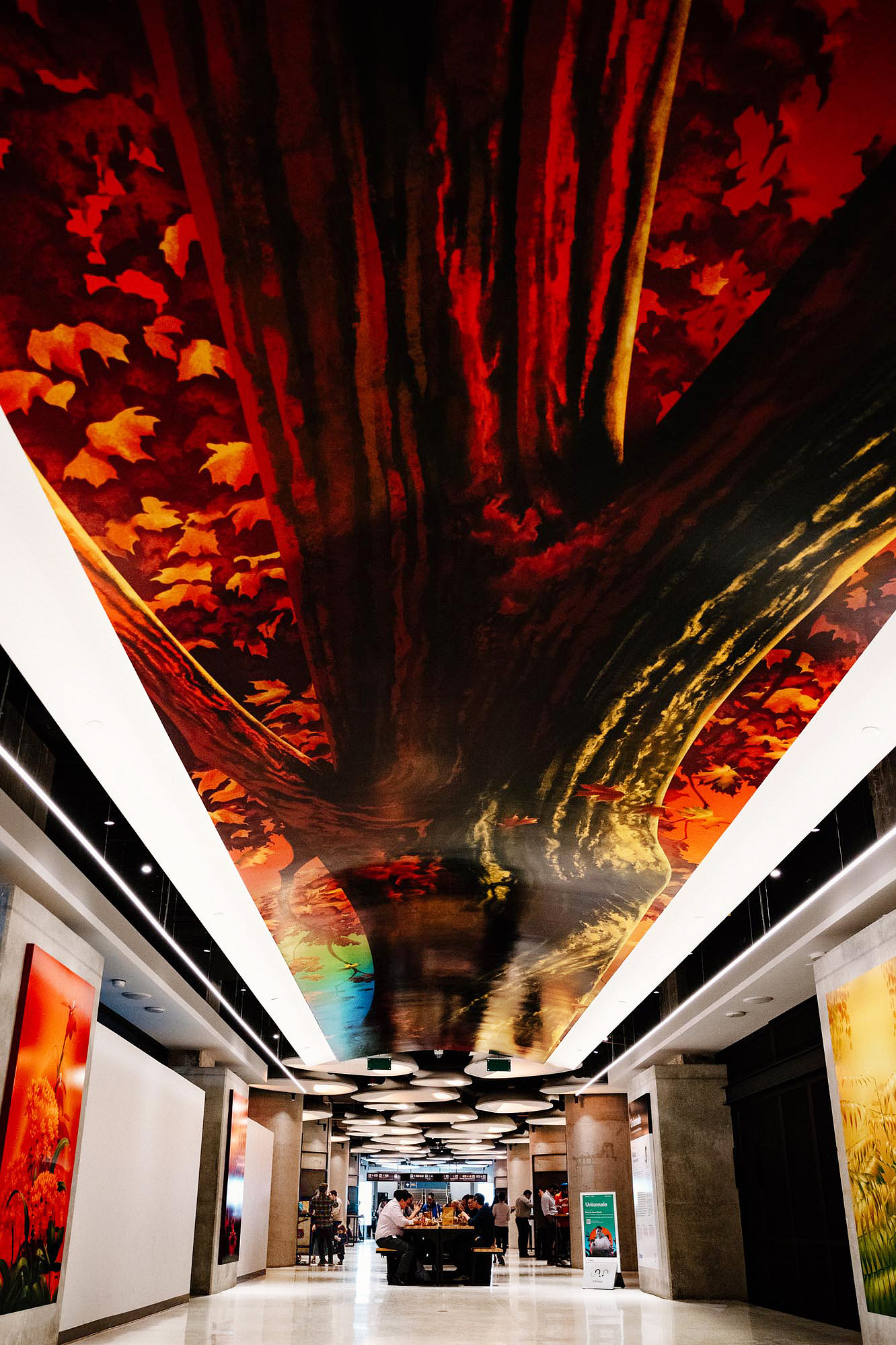 A large tree mural is above a ceiling vault in a public space with nature-inspired artworks on the walls.
