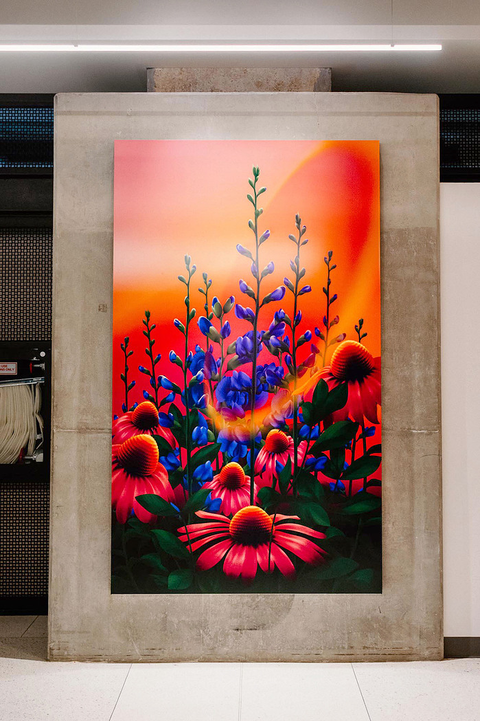 A vibrant artwork featuring red, pink, and purple flowers and plants is displayed on a wall.