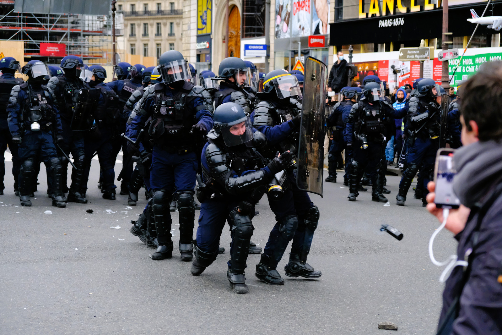 Un gendarme mobile jette une grenade de désencerclement au milieu de la foule. 