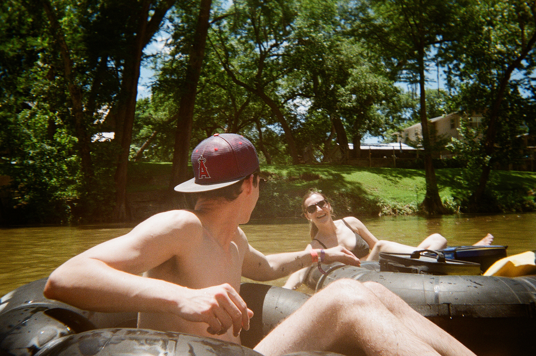 Diego and I, with Diego's head turned backwards, both sitting in tubes in the murky Comal River on a sunny day.
