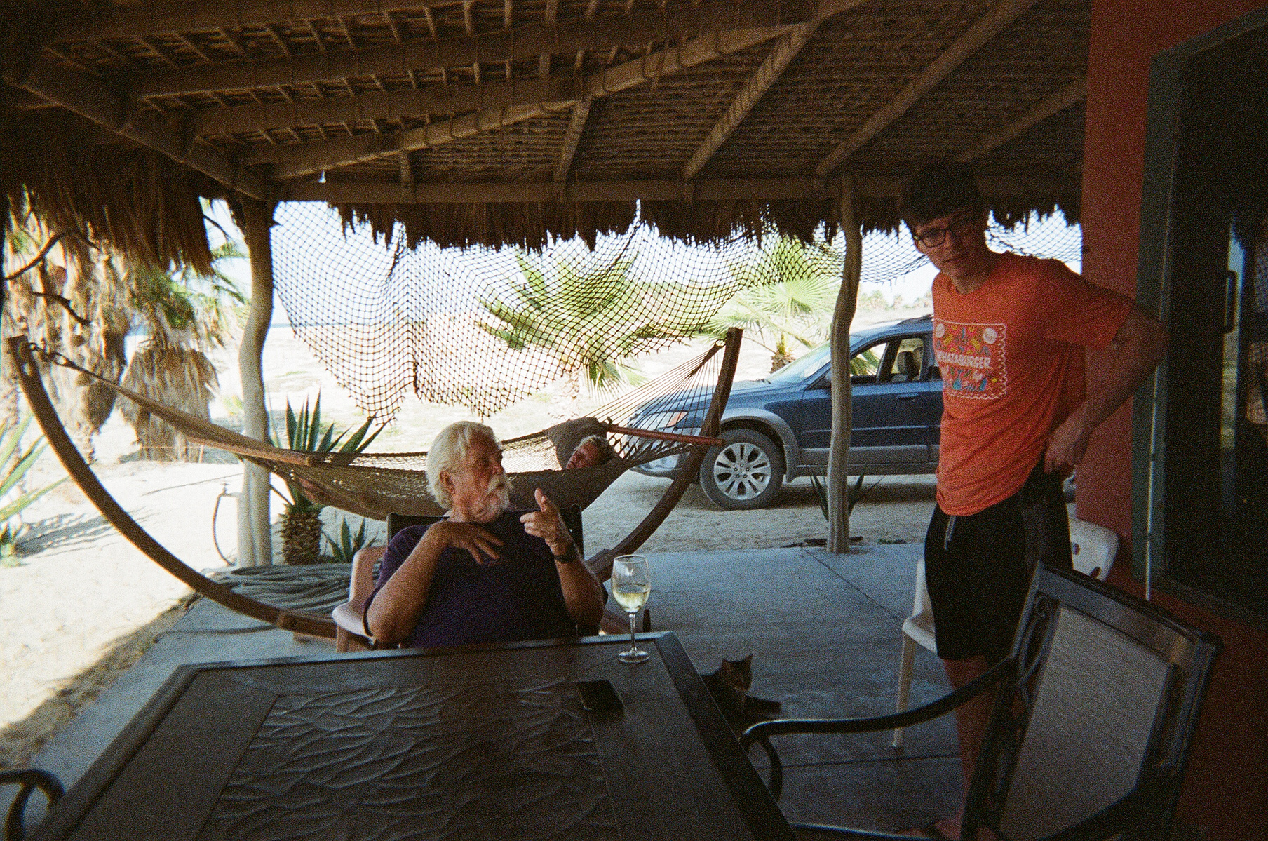 Clarence and Diego sitting on the beach porch with a palapa roof and hammock in background.