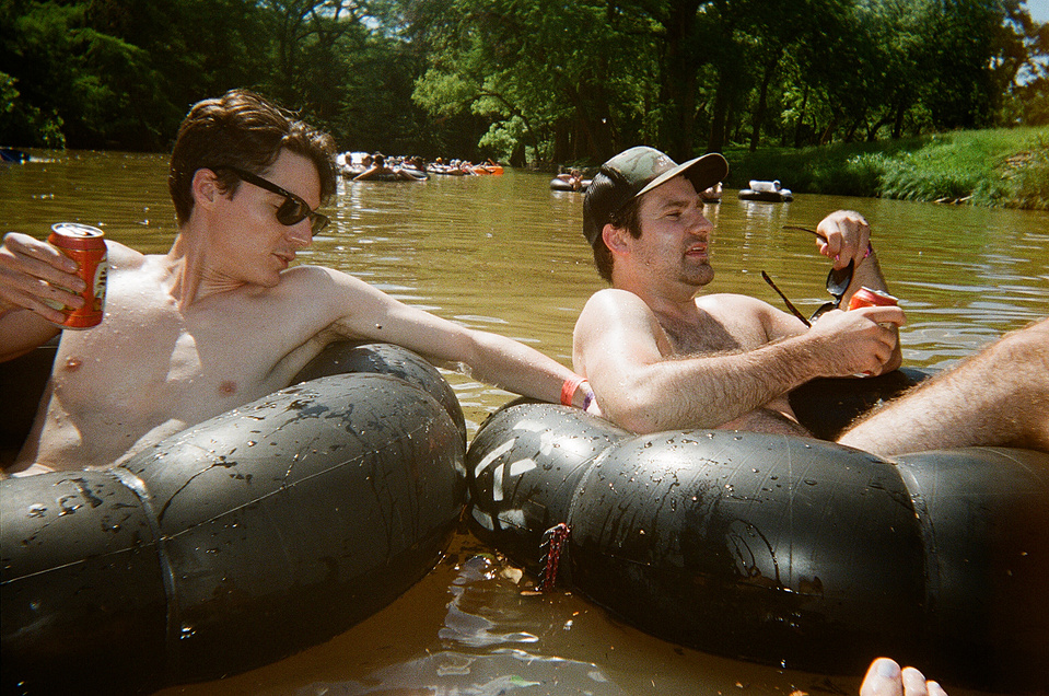 Two young guys sitting on innertubes, floating the Comal River.