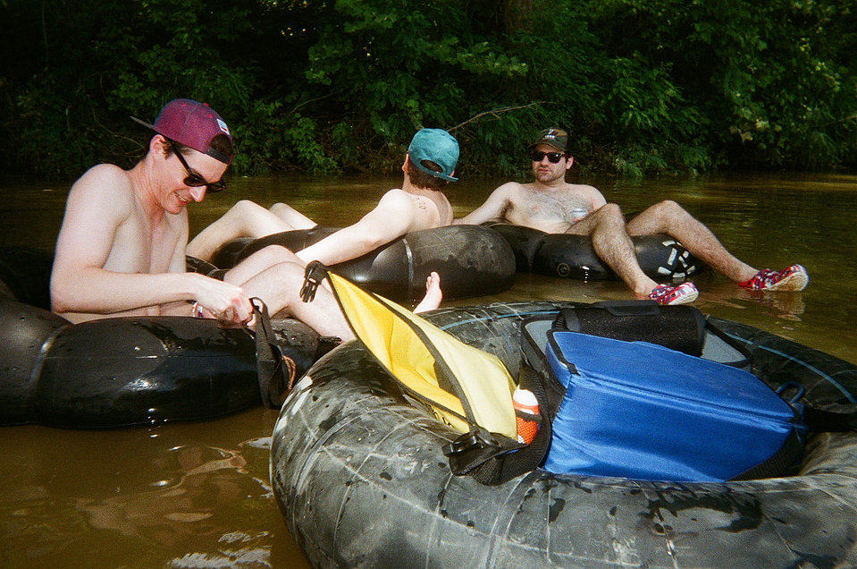 Three young guys - with really white legs - sitting on innertubes, floating the Comal River, with an additional tube towing our coolers.