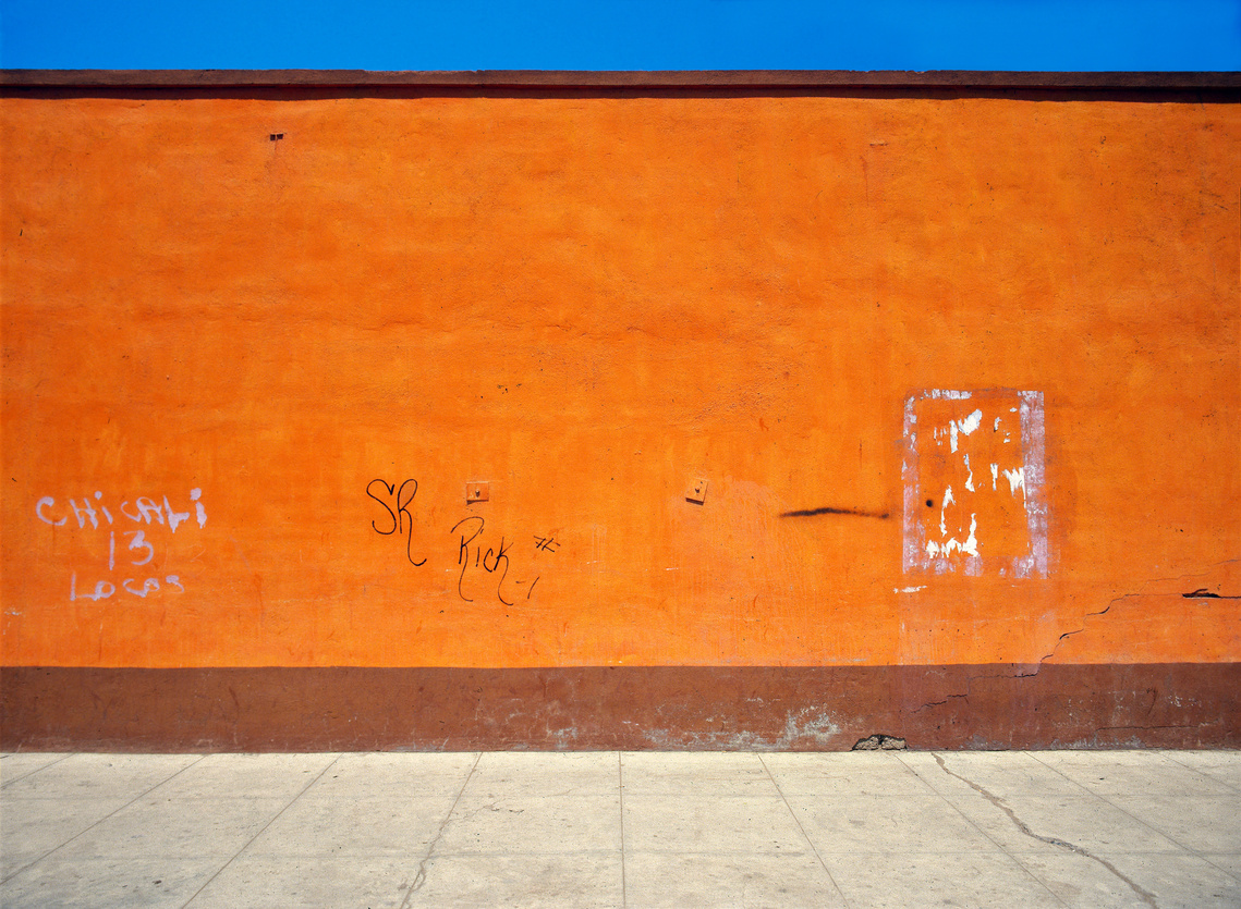 From George Bedell’s Wasteland Series. Fine art photograph of bright orange-red wall, grey sidewalk, and deep blue sky in Baja California, Mexico. 1985.