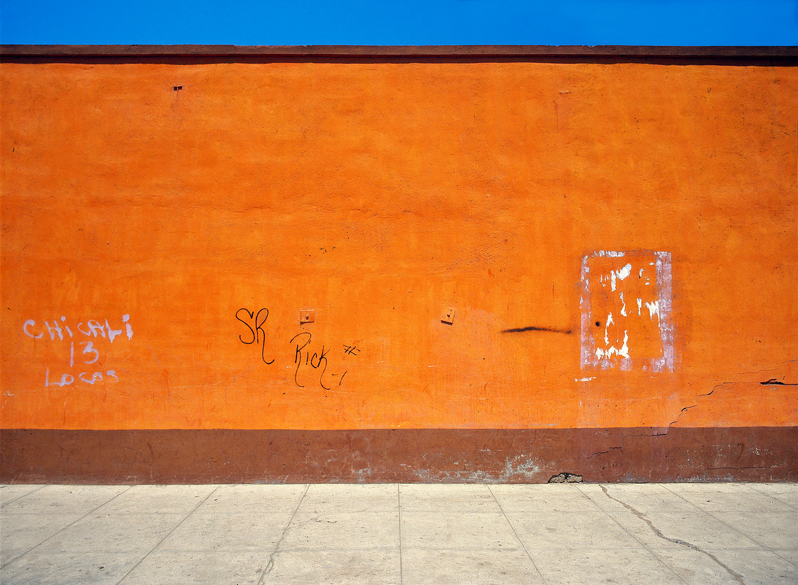 From George Bedell’s Wasteland Series. Fine art photograph of bright orange-red wall, grey sidewalk, and deep blue sky in Baja California, Mexico. 1985.