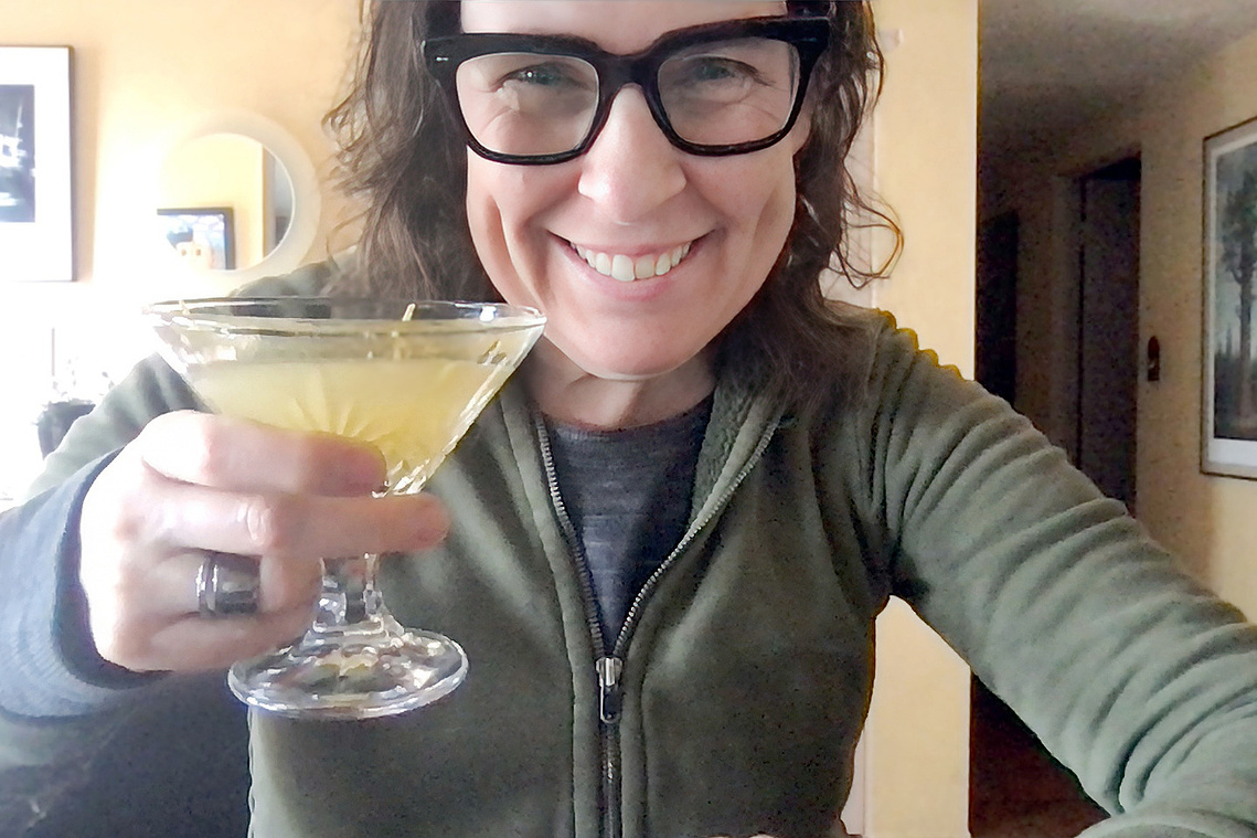 Portrait of The Unofficial Yellowstone Cookbook author Jackie Alpers holding The Bee's Knees cocktail from 1923