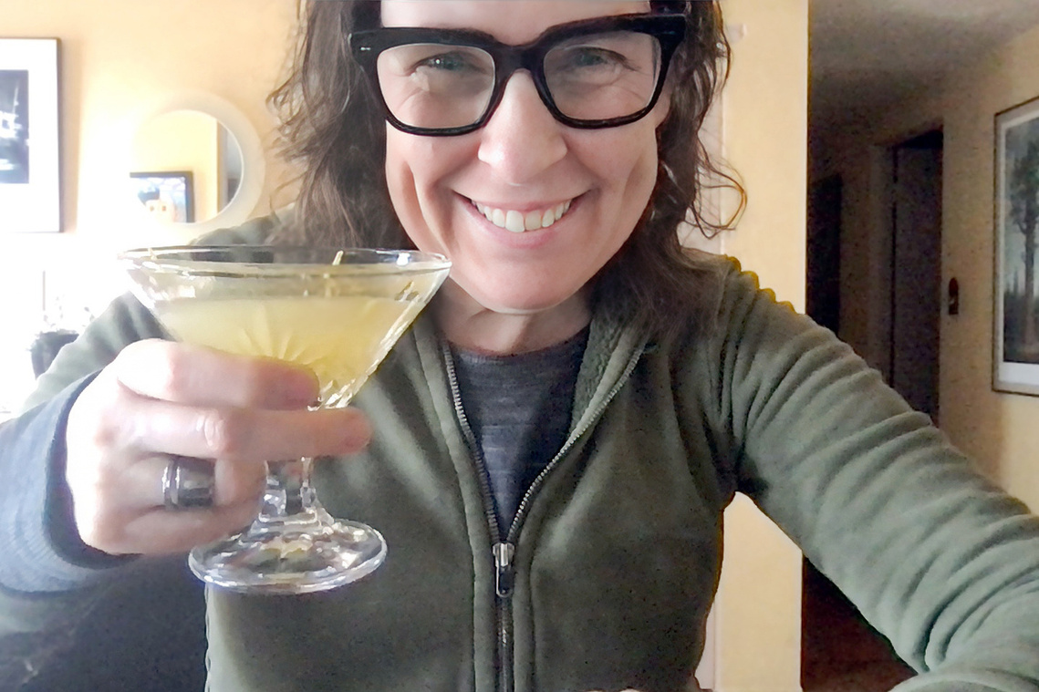 Portrait of The Unofficial Yellowstone Cookbook author Jackie Alpers holding The Bee's Knees cocktail from 1923