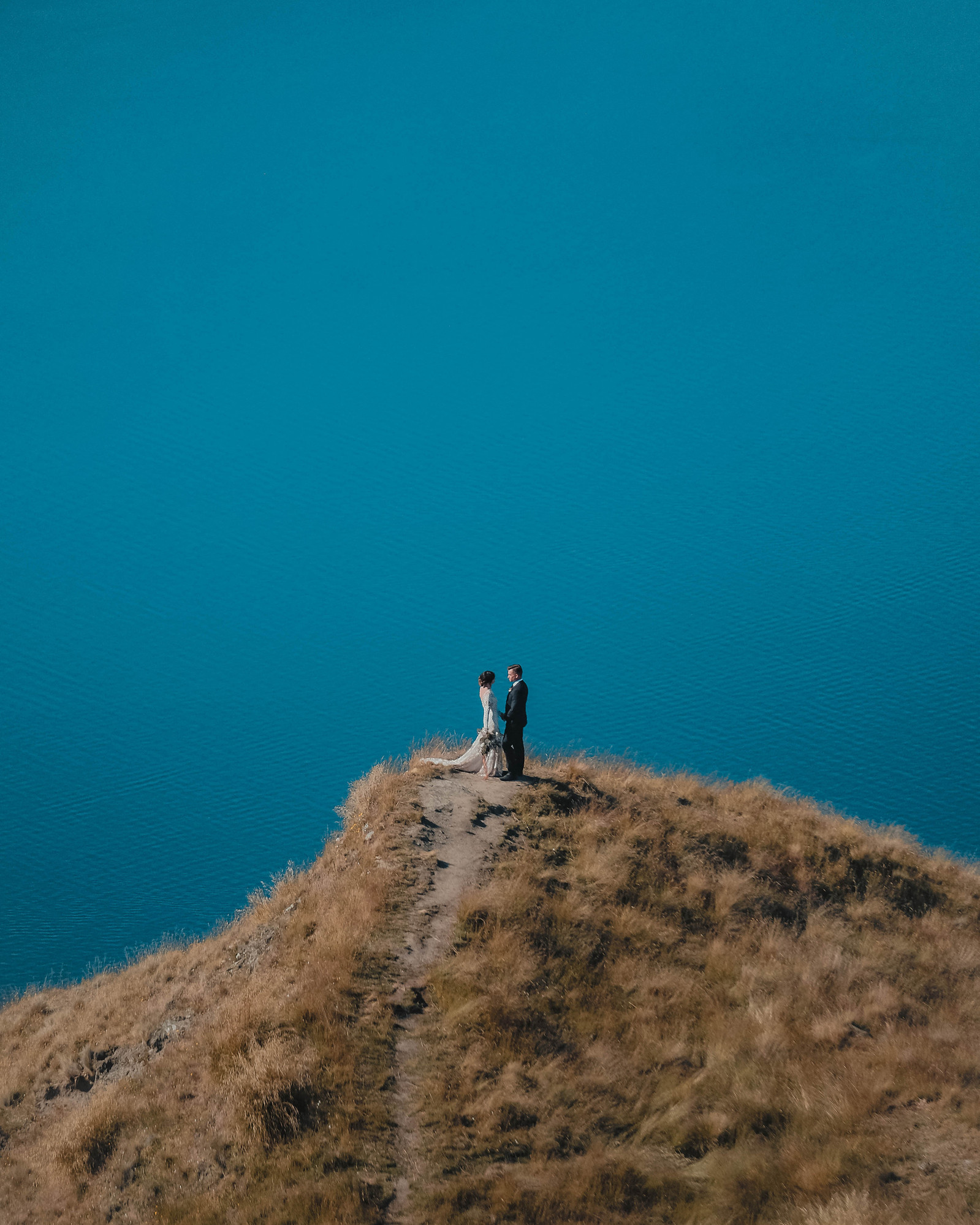 A newly wed couple stands alone on the edge of a cliff, shortly after the elopement ceremony in Wanaka, New Zealand