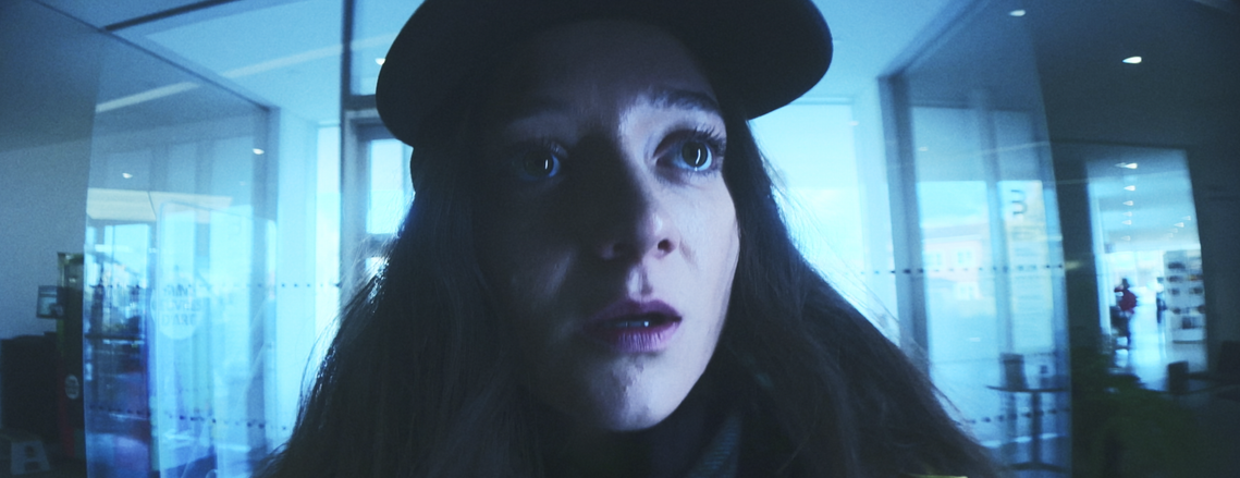 Film banner for Something's Not Quite Right (2024), a psychological horror by Simon Klinger. The image shows the protagonist's fearful expression in a sterile, cold-toned environment, with a wide frame emphasizing her vulnerability.