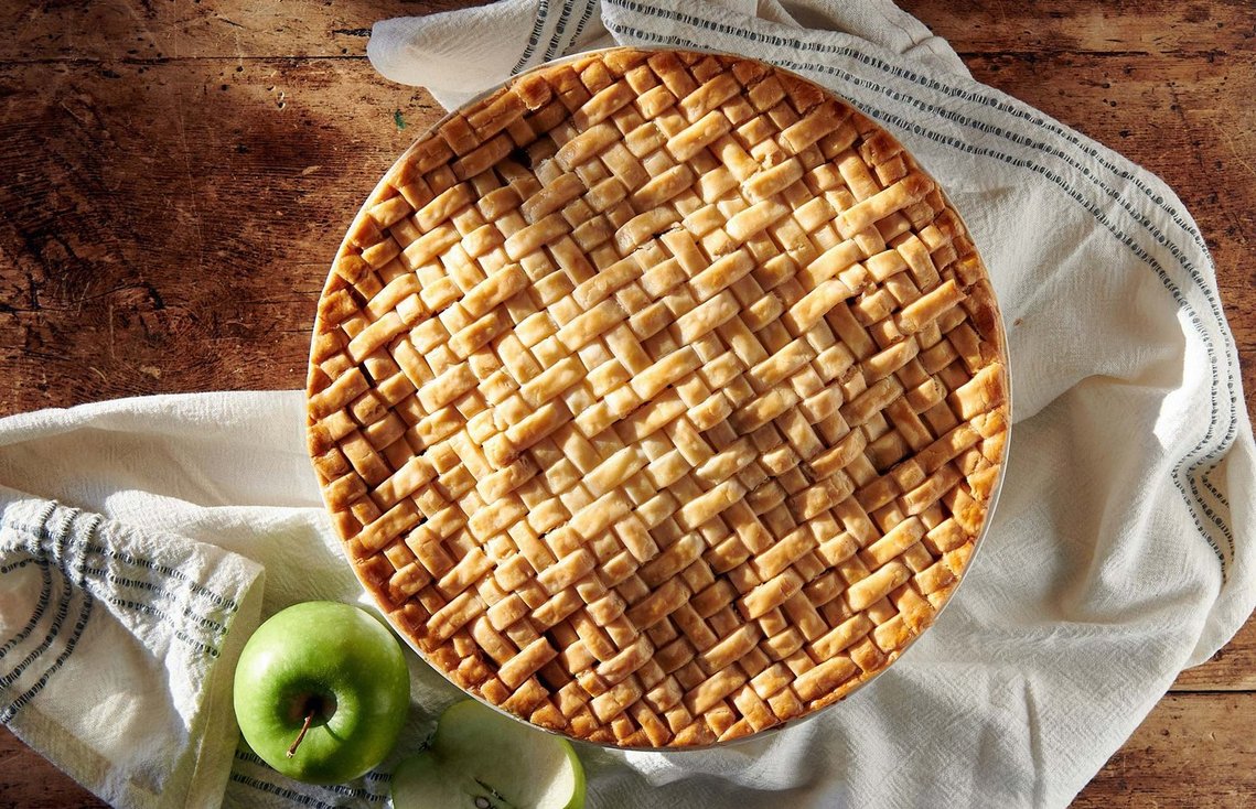 an intricate lattice-woven apple pie on a weathered wooden farm table, with a muslin cloth draped around the pie dish