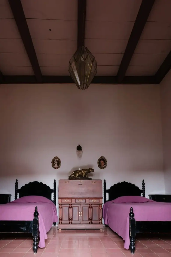 A glass lantern from the studio of Mauricio Preciado in the town of Tlaquepaque hangs over twin beds carved by Muñiz and topped with mauve bedcovers woven in Oaxaca for Estudio Pomelo. Credit Ana Topoleanu