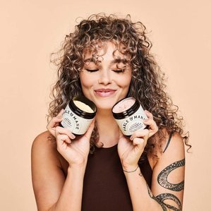 Fable &amp;amp; Mane hair mask and purifying scrub being held by tattooed model with curly hair. Photographed in a London studio