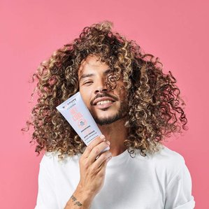 Curly haired male model holding Noughty hair care Hey curl scrunching jelly. Photographed and styled by cosmetic photographer Tom Hargreaves in his studio in Exeter, Devon