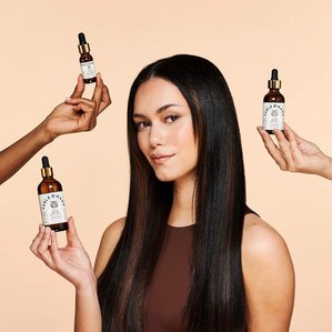 Fable &amp;amp;amp;amp; Mane hair oil in three sizes being held by model plus two other models arms coming in from the side. Photographed by Tom Hargreaves in a London studio